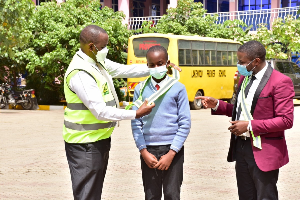 Automobile Association of Kenya CEO Francis Theuri shows Lakewood Premier class 7 student Jerome Thomas how to wear a reflective to mark start of pedestrian visibility campaign targeting 20,000 children.